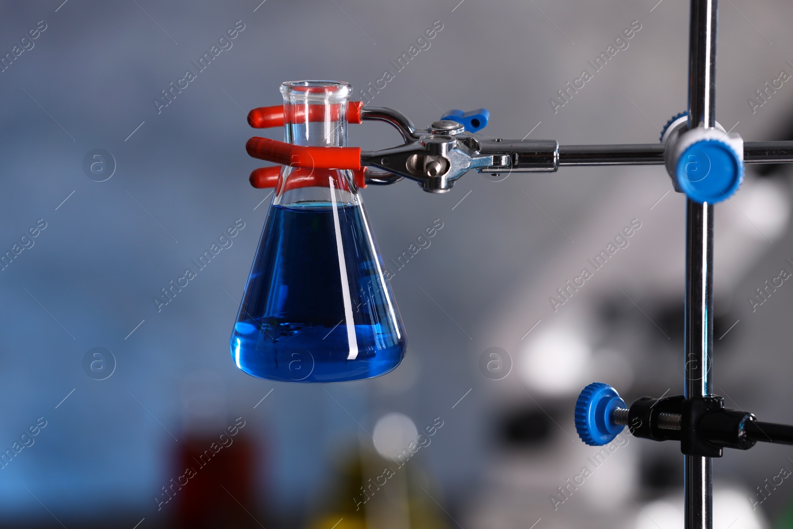 Photo of Flask with blue liquid on retort stand in laboratory, closeup