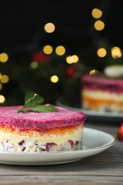 Herring under fur coat salad on white wooden table against blurred festive lights, closeup with space for text. Traditional Russian dish