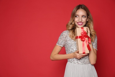 Happy woman with gift box on red background, space for text. Christmas party