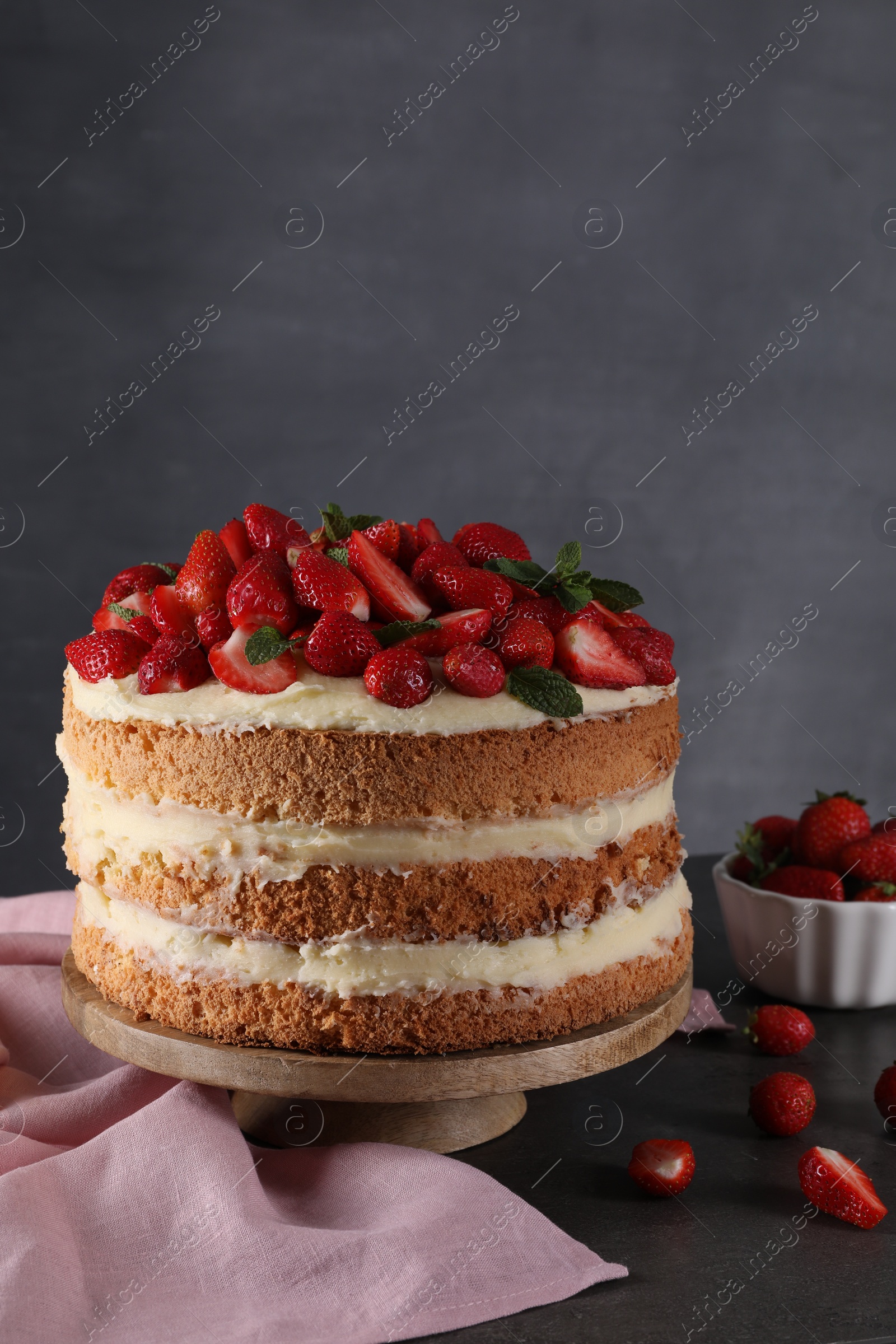 Photo of Tasty cake with fresh strawberries and mint on table against dark gray background