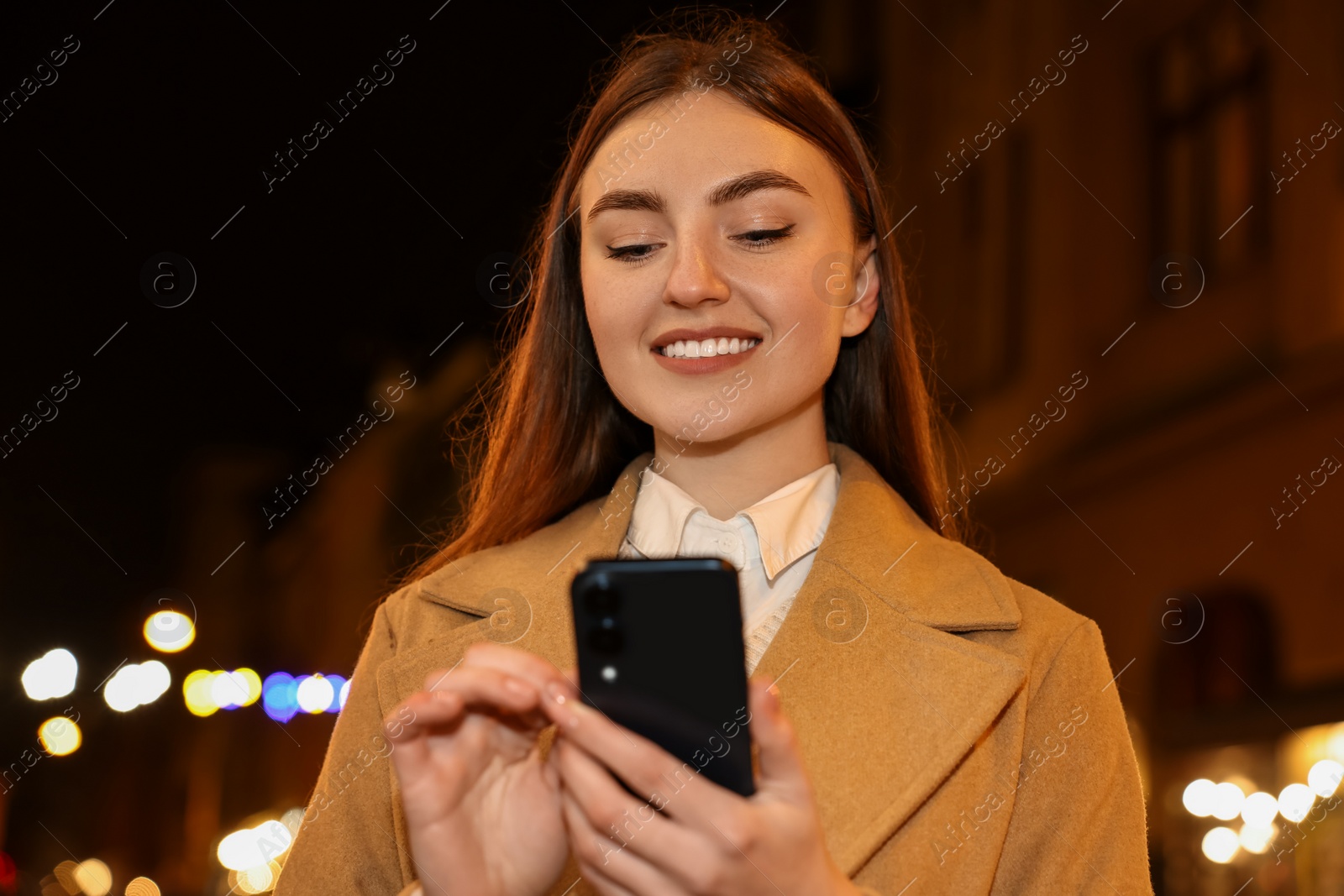 Photo of Smiling woman using smartphone on night city street