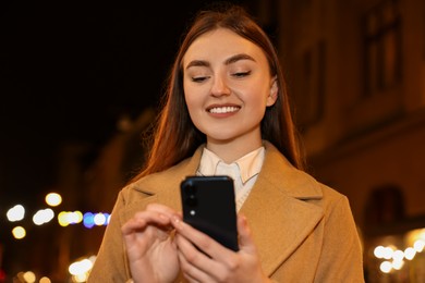 Smiling woman using smartphone on night city street