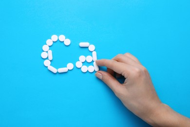 Woman making calcium symbol with white pills on light blue background, top view
