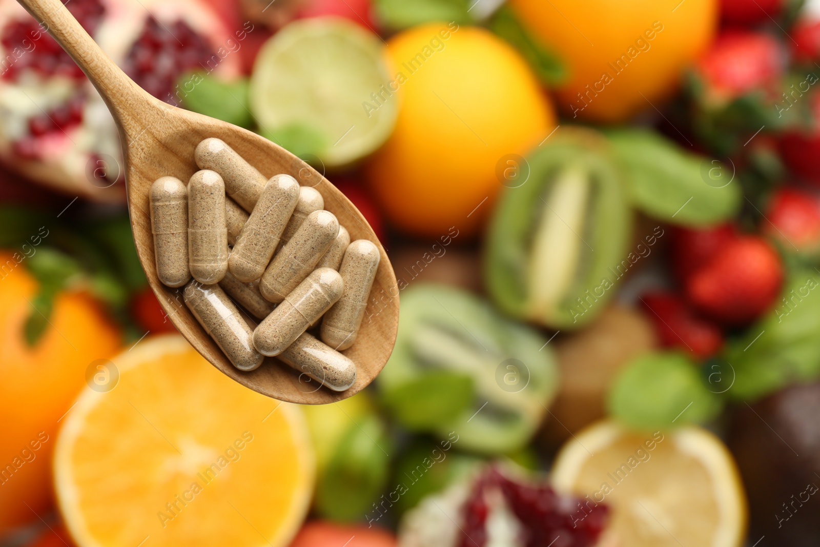 Photo of Vitamin pills in spoon over fresh fruits, top view. Space for text