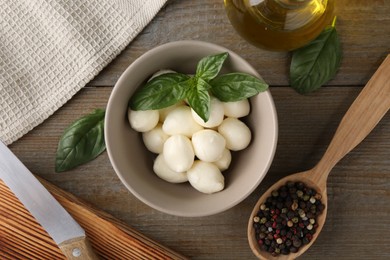 Photo of Tasty mozarella balls, basil leaves, oil and spices on wooden table, flat lay