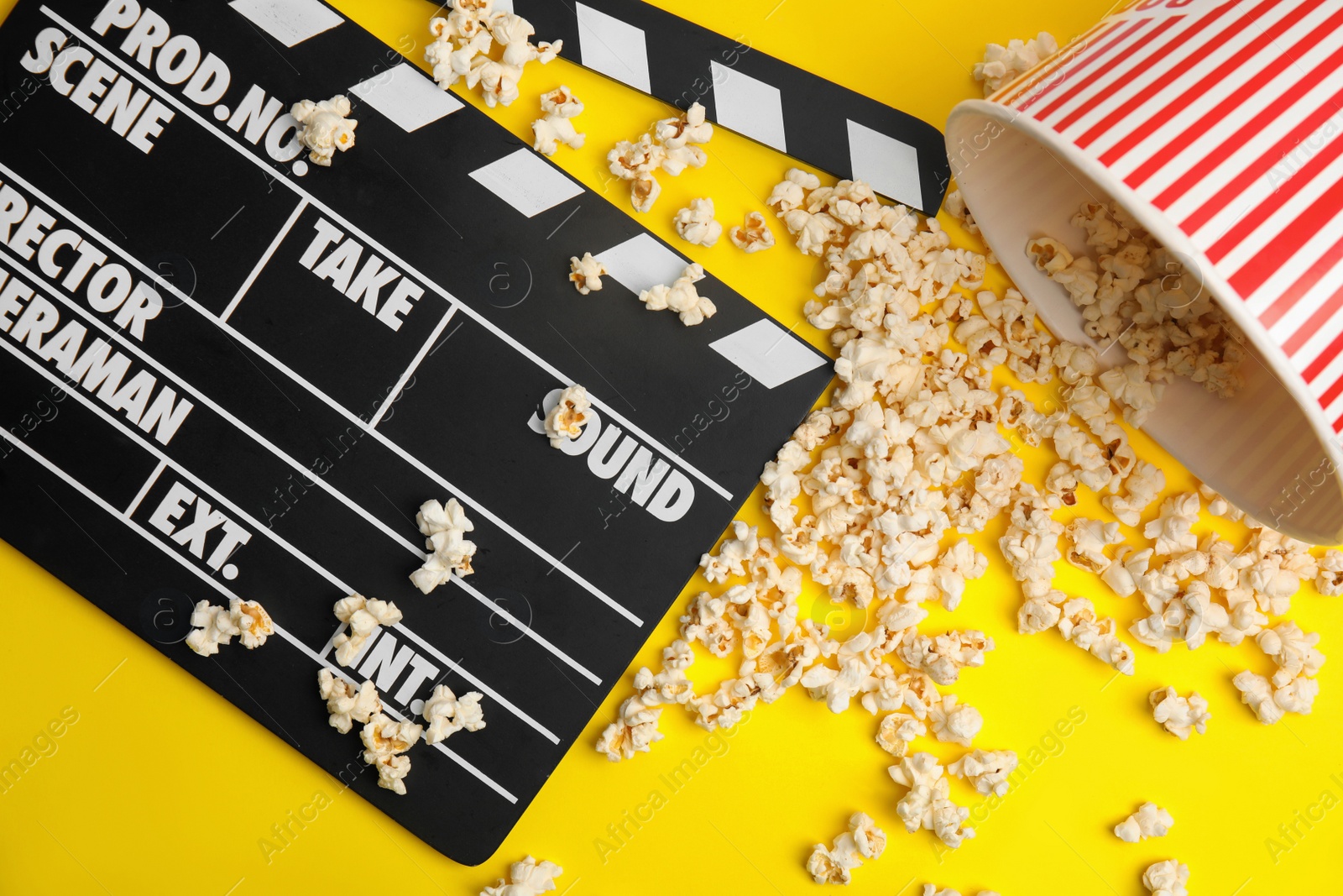 Photo of Tasty pop corn and clapboard on yellow background, flat lay
