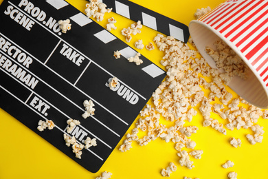 Photo of Tasty pop corn and clapboard on yellow background, flat lay