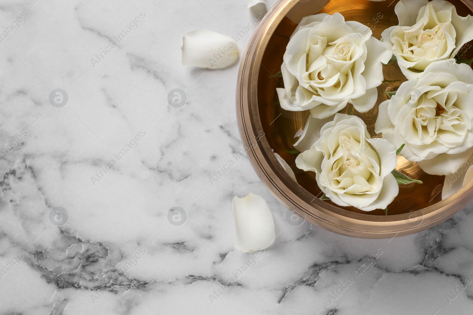 Photo of Tibetan singing bowl with water and beautiful roses on white marble table, top view. Space for text