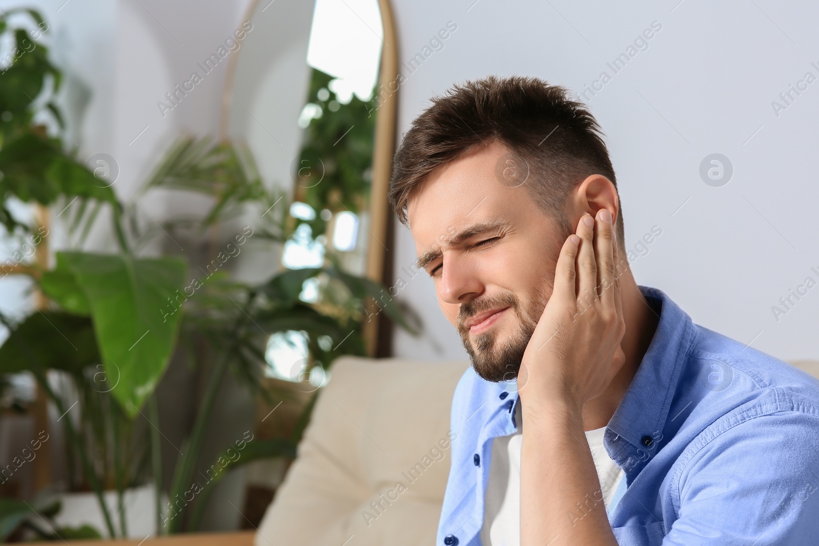 Photo of Young man suffering from ear pain at home. Space for text