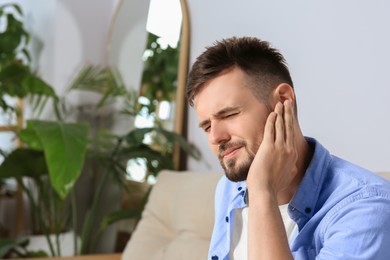 Photo of Young man suffering from ear pain at home. Space for text