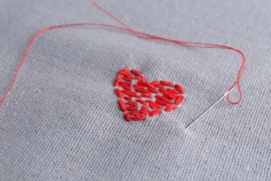 Embroidered red heart and needle on gray cloth, closeup