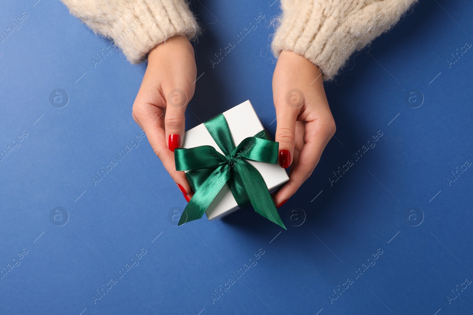 Photo of Christmas present. Woman with gift box on blue background, top view