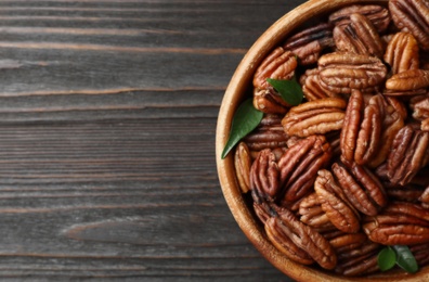 Photo of Dish with shelled pecan nuts on wooden background, top view. Space for text