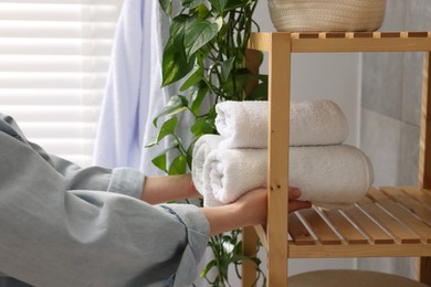 Photo of Woman putting rolled towels onto shelf indoors, closeup