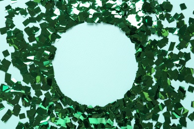 Frame of shiny green confetti on cyan background, flat lay. Space for text