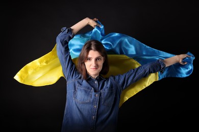 Photo of Young woman holding Ukrainian flag on black background