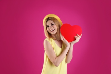 Beautiful woman with paper heart on color background