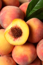 Cut and whole fresh ripe peaches with green leaves as background, top view