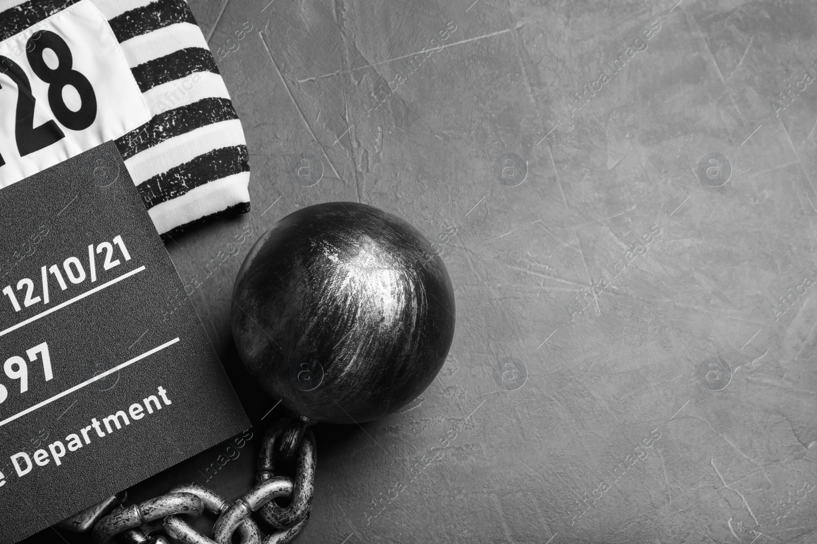 Photo of Metal ball with chain, prison uniform and mugshot letter board on grey table, flat lay. Space for text