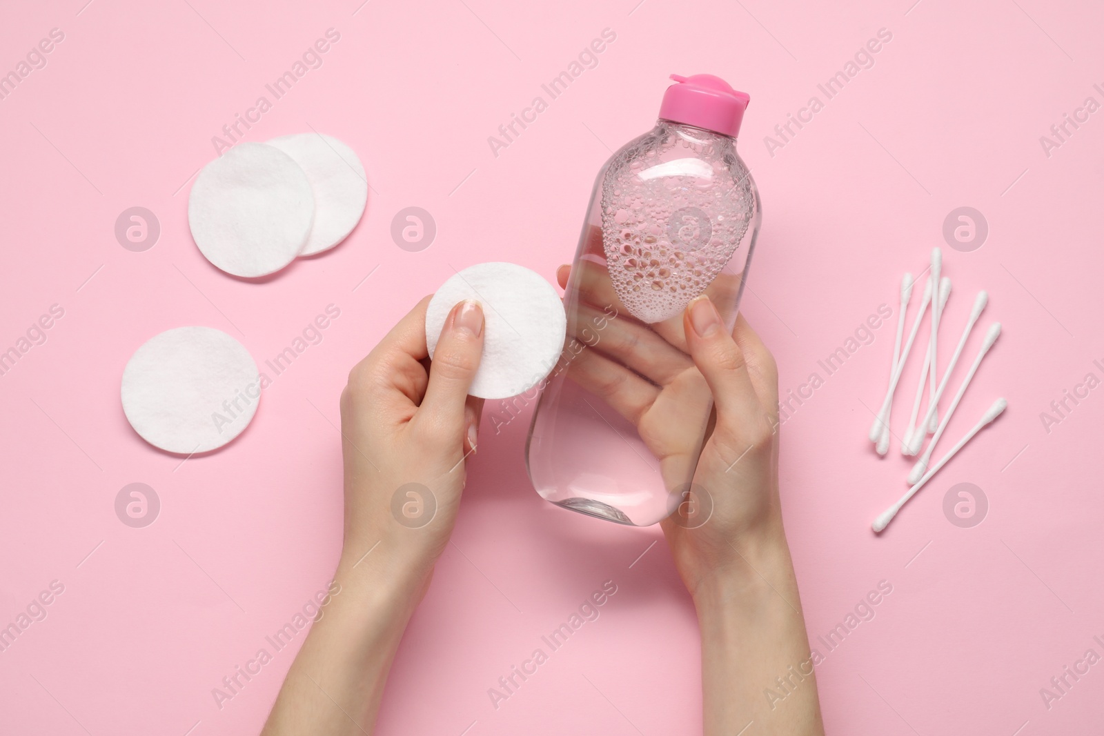 Photo of Woman holding makeup remover and cotton pad on pink background, top view