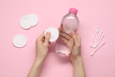 Photo of Woman holding makeup remover and cotton pad on pink background, top view