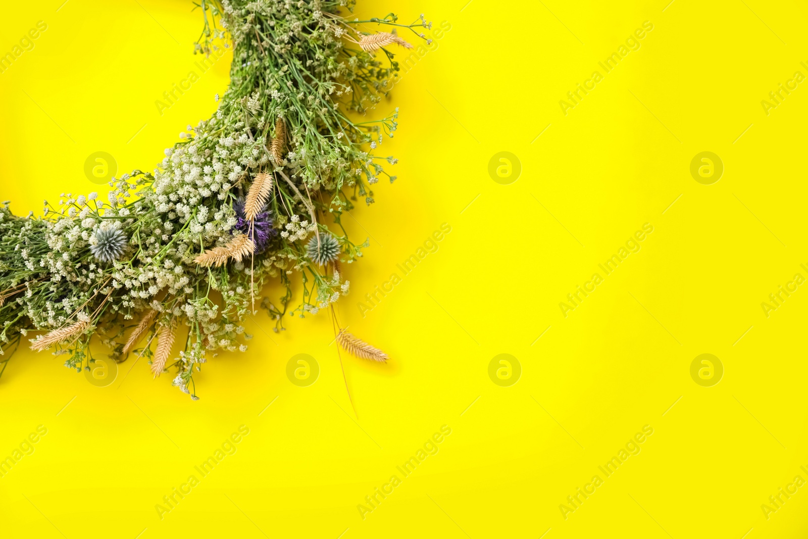 Photo of Beautiful wreath made of wildflowers on yellow background, top view. Space for text