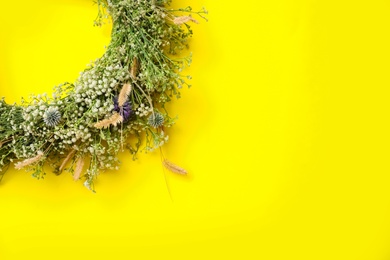 Beautiful wreath made of wildflowers on yellow background, top view. Space for text