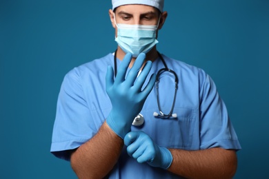 Photo of Doctor in protective mask putting on medical gloves against blue background