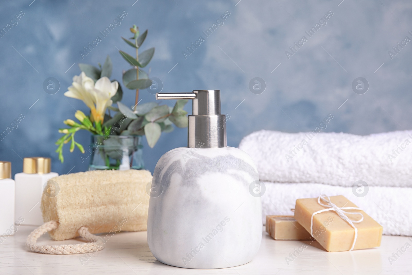 Photo of Marble dispenser, soap bars and luffa sponge on white wooden table