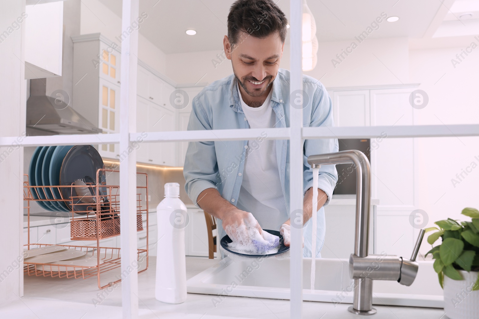 Photo of Man washing plate above sink in kitchen, view from outside