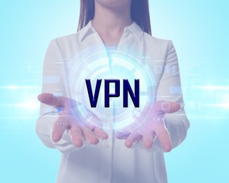 Woman holding virtual icon VPN on light blue background, closeup