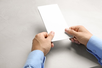 Photo of Young man holding blank brochure at grey table, closeup. Mock up for design