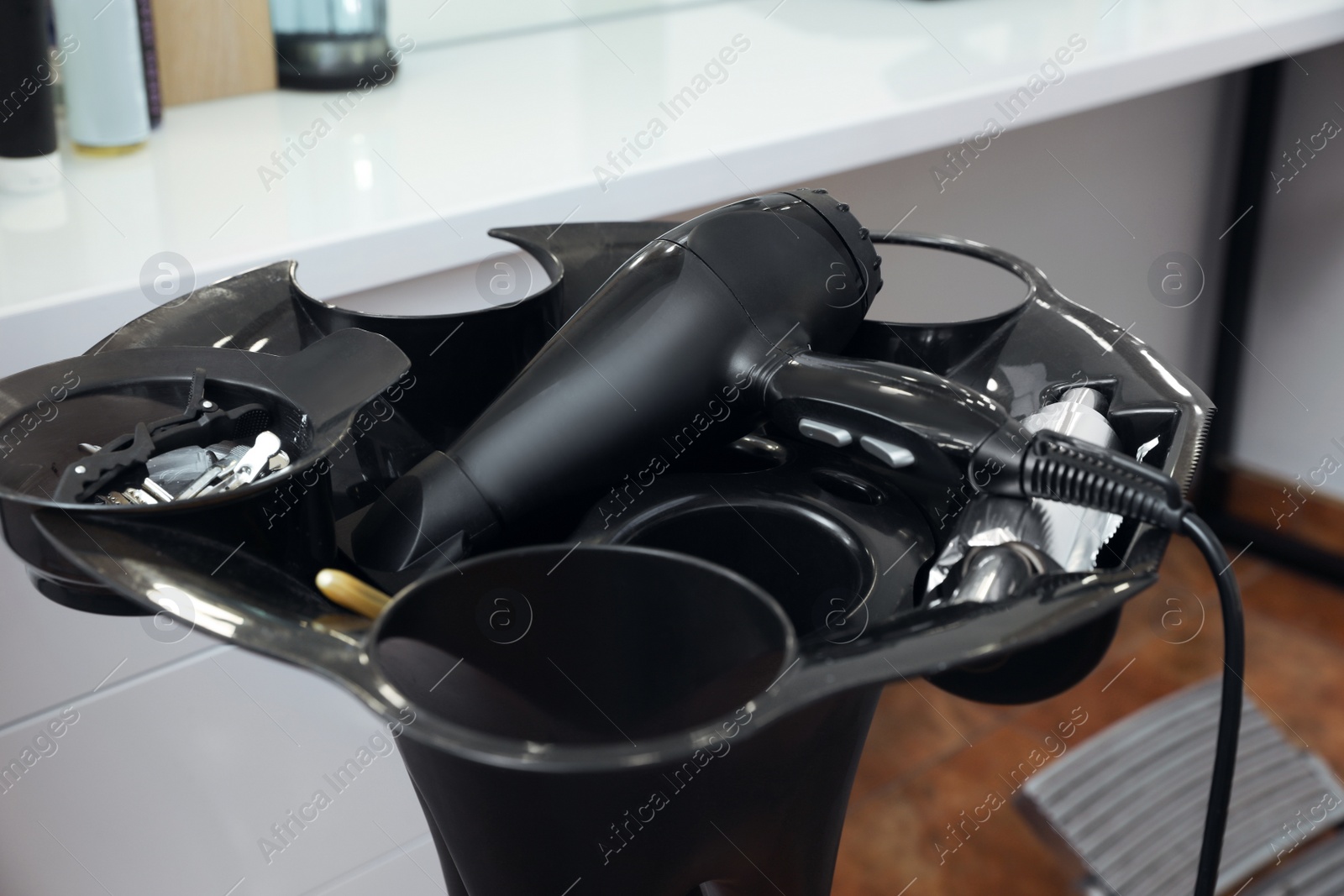 Photo of Modern hair dryer and clips on stand in beauty salon