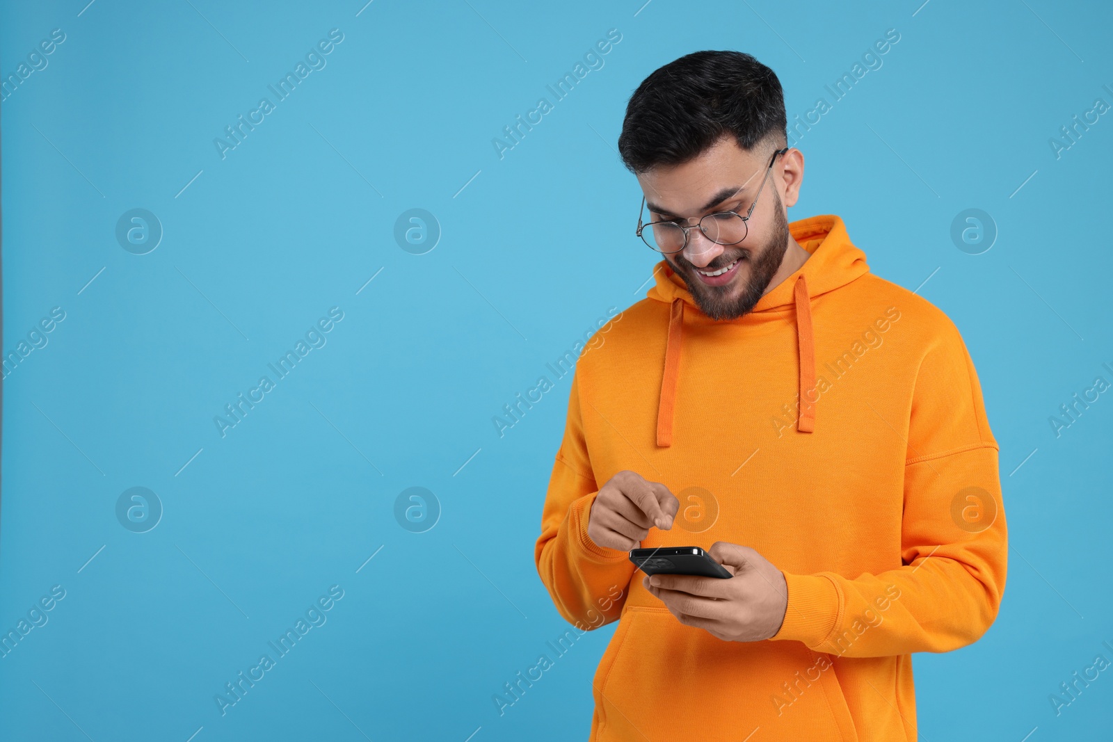 Photo of Happy young man using smartphone on light blue background, space for text