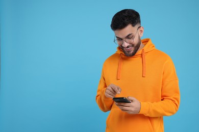 Photo of Happy young man using smartphone on light blue background, space for text