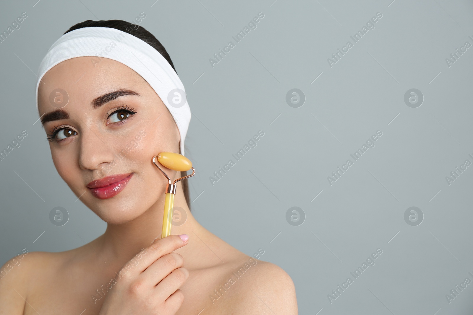 Photo of Woman using natural jade face roller on grey background, space for text
