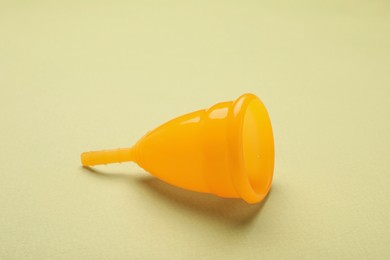 Photo of Orange menstrual cup on light green background, closeup