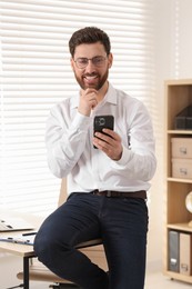 Photo of Portrait of smiling man with smartphone in office