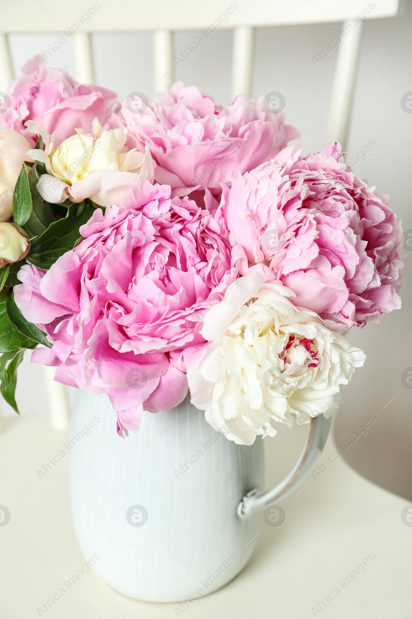 Photo of Beautiful peonies in jug on white chair, closeup