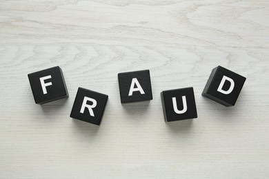 Photo of Black cubes with word Fraud on white wooden table, flat lay