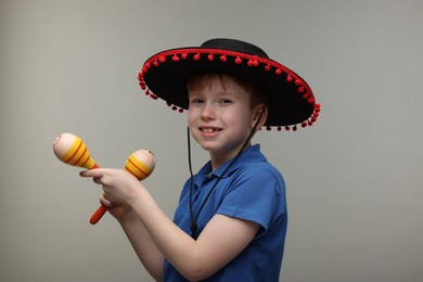 Photo of Cute boy in Mexican sombrero hat with maracas on grey background
