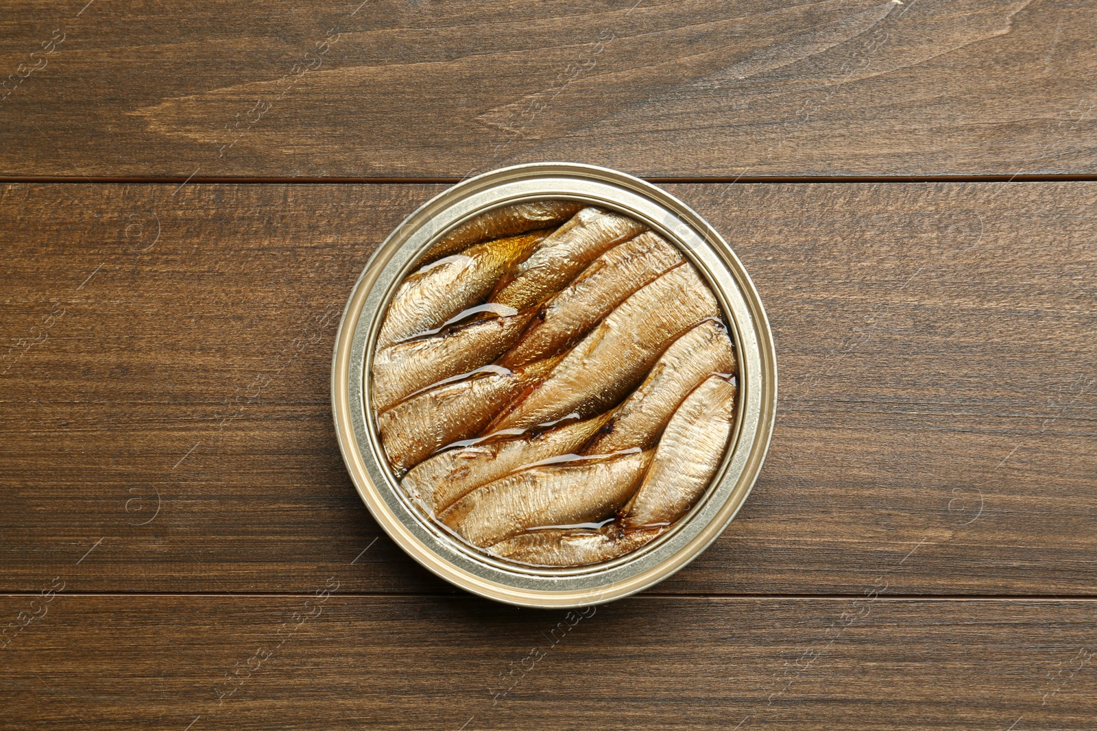 Photo of Sprats in tin can on wooden table, top view