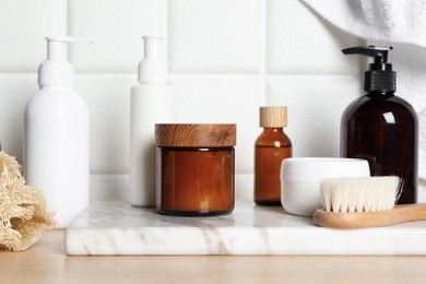 Photo of Different bath accessories and personal care products on wooden table near white tiled wall