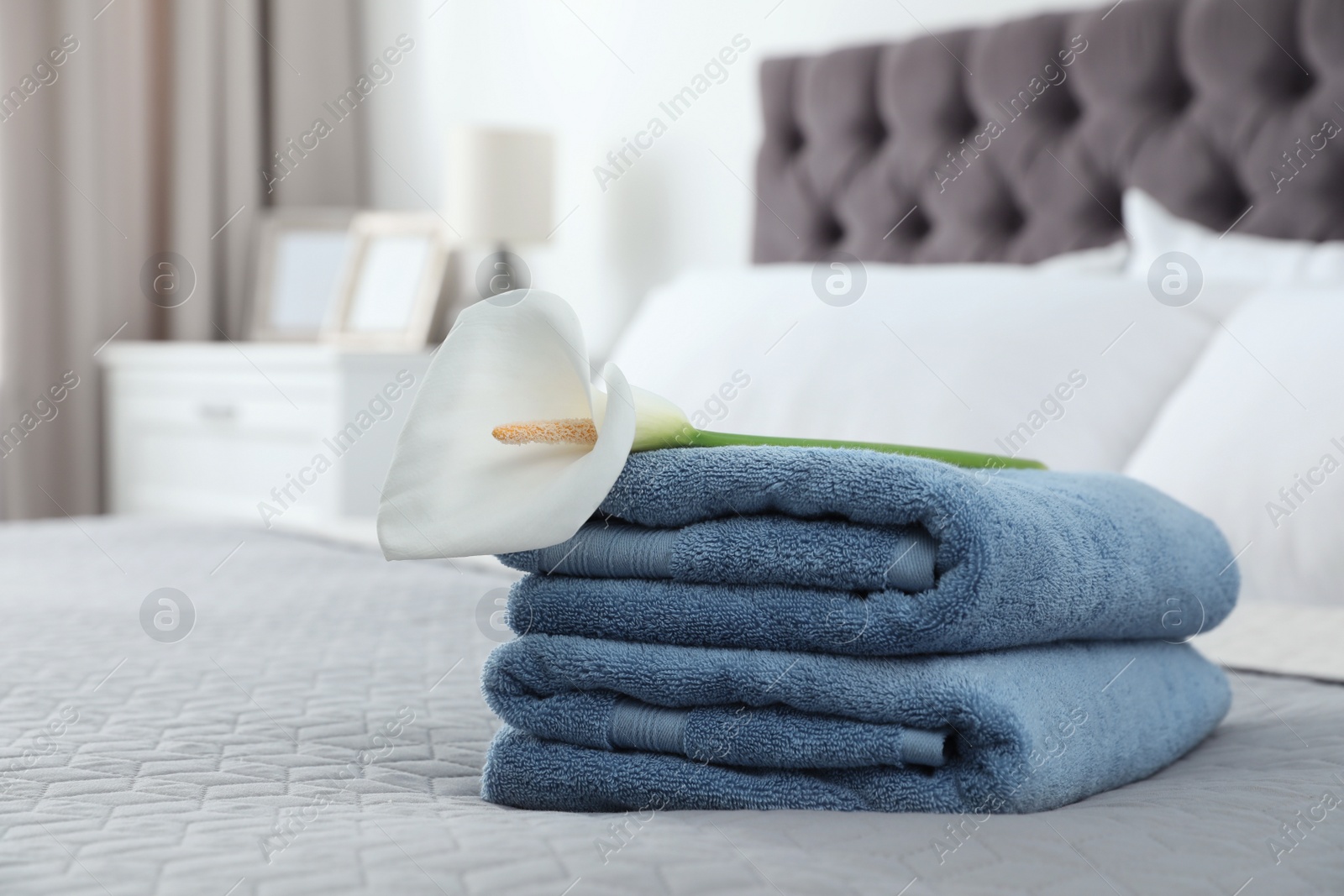 Photo of Stack of clean towels with flower on bed indoors