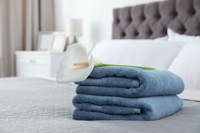 Stack of clean towels with flower on bed indoors