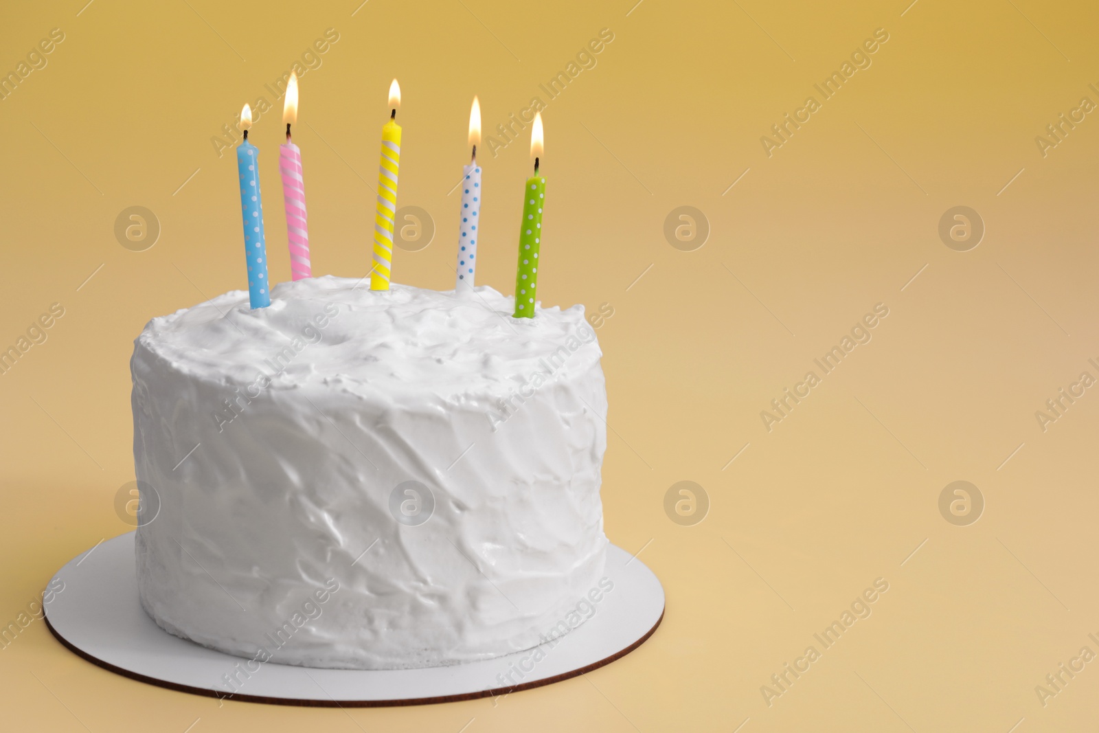 Photo of Delicious cake with cream and burning candles on yellow background. Space for text