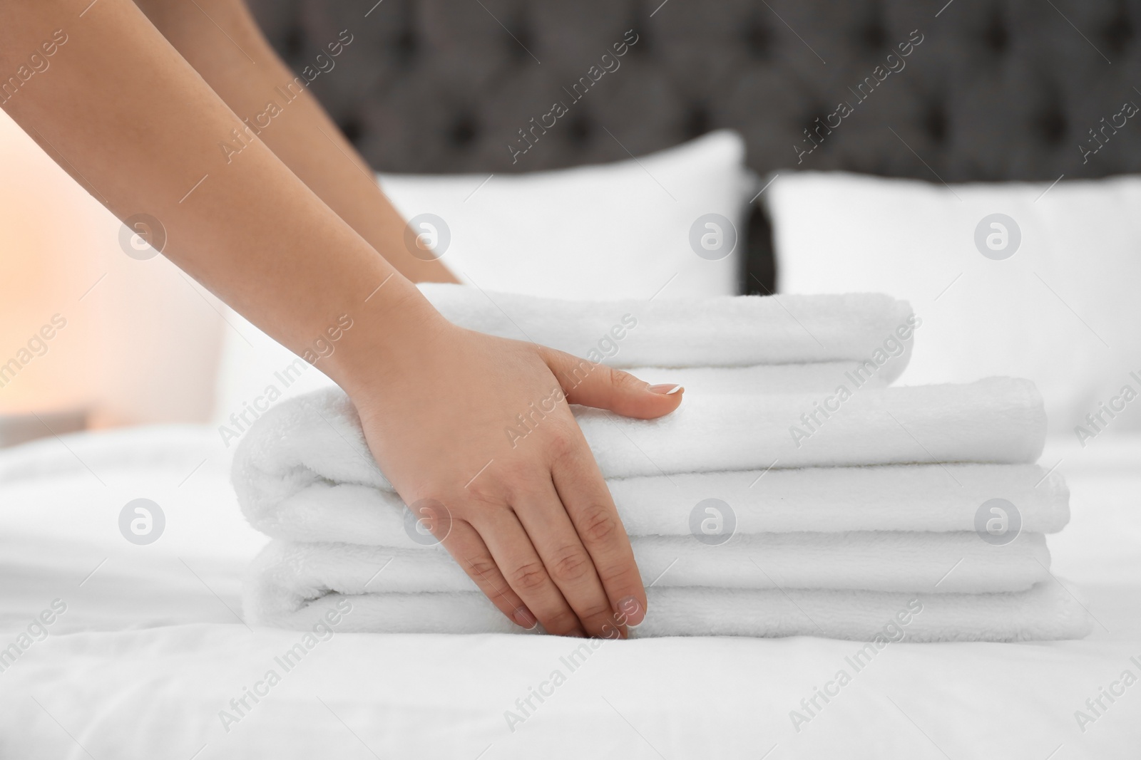 Photo of Chambermaid with stack of towels on bed in hotel room