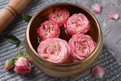 Photo of Tibetan singing bowl with water, beautiful roses and mallet on grey textured table, closeup