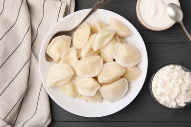 Photo of Delicious dumplings (varenyky) with cottage cheese served on black wooden table, flat lay