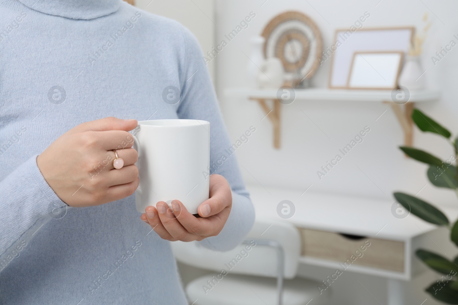 Photo of Woman holding white mug at home, closeup and space for text. Mockup for design